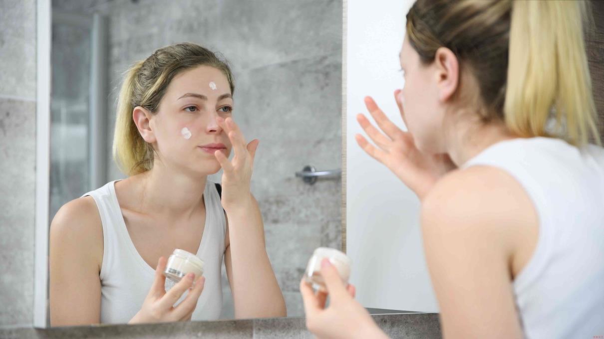Young woman applying face cream in the mirror