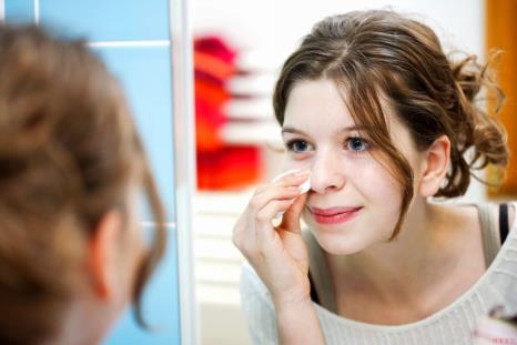Teenage girl cleaning her face in the mirror