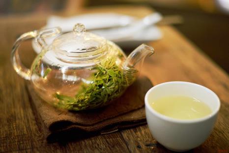 A glass teapot of green tea with a cup of green tea beside it.