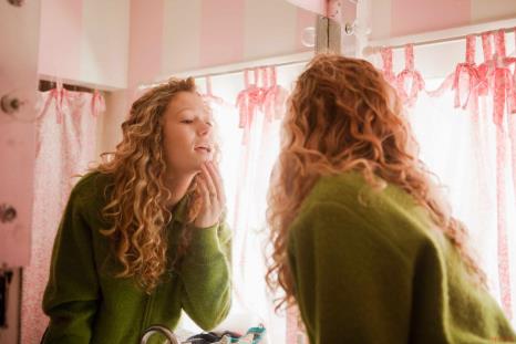 Young woman examining her skin in the bathroom mirror