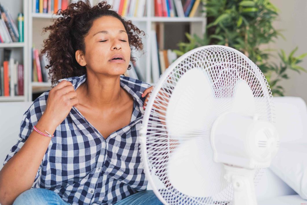 Woman opening shirt in front of table fan