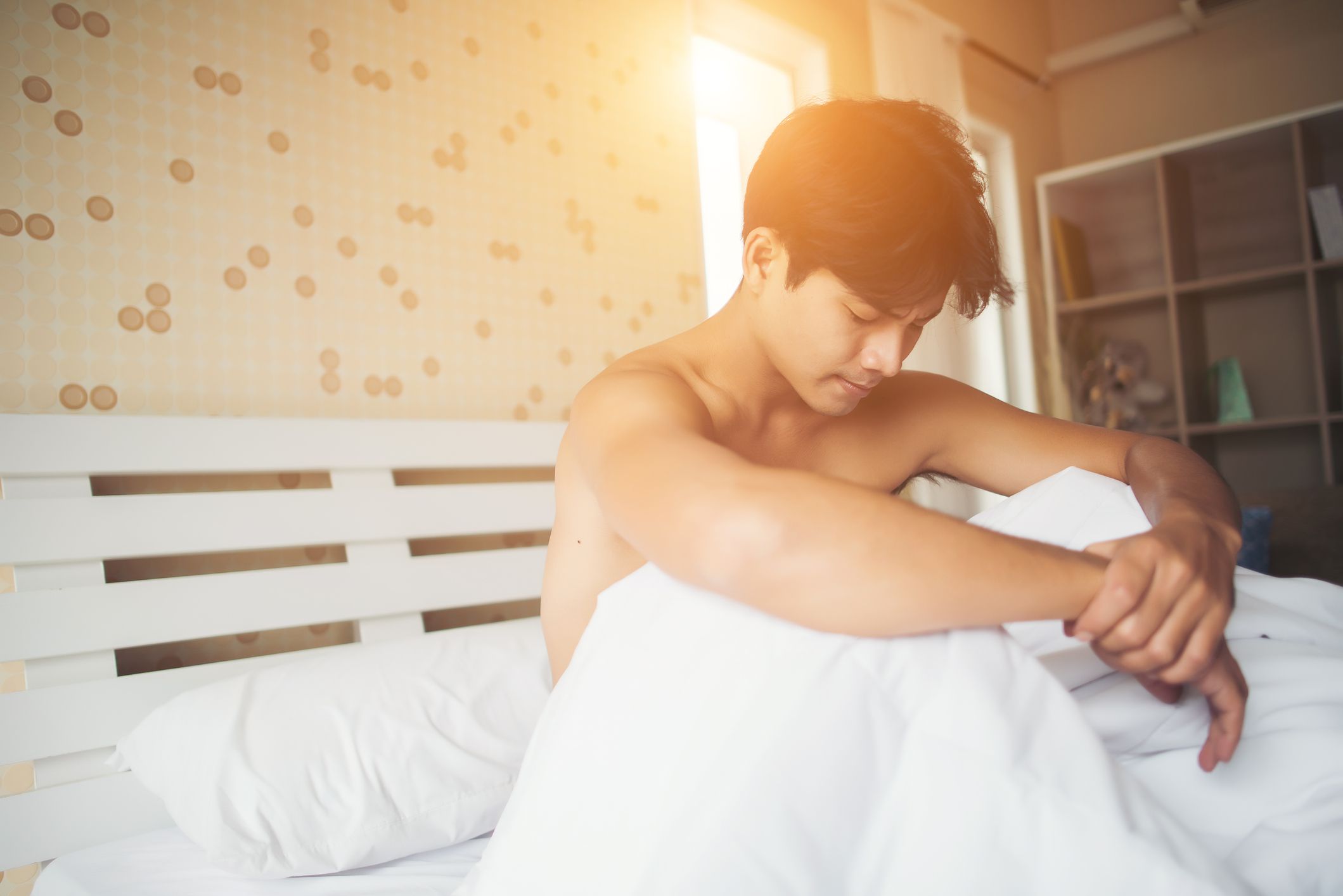 A shirtless young man siting on his bed at sunset