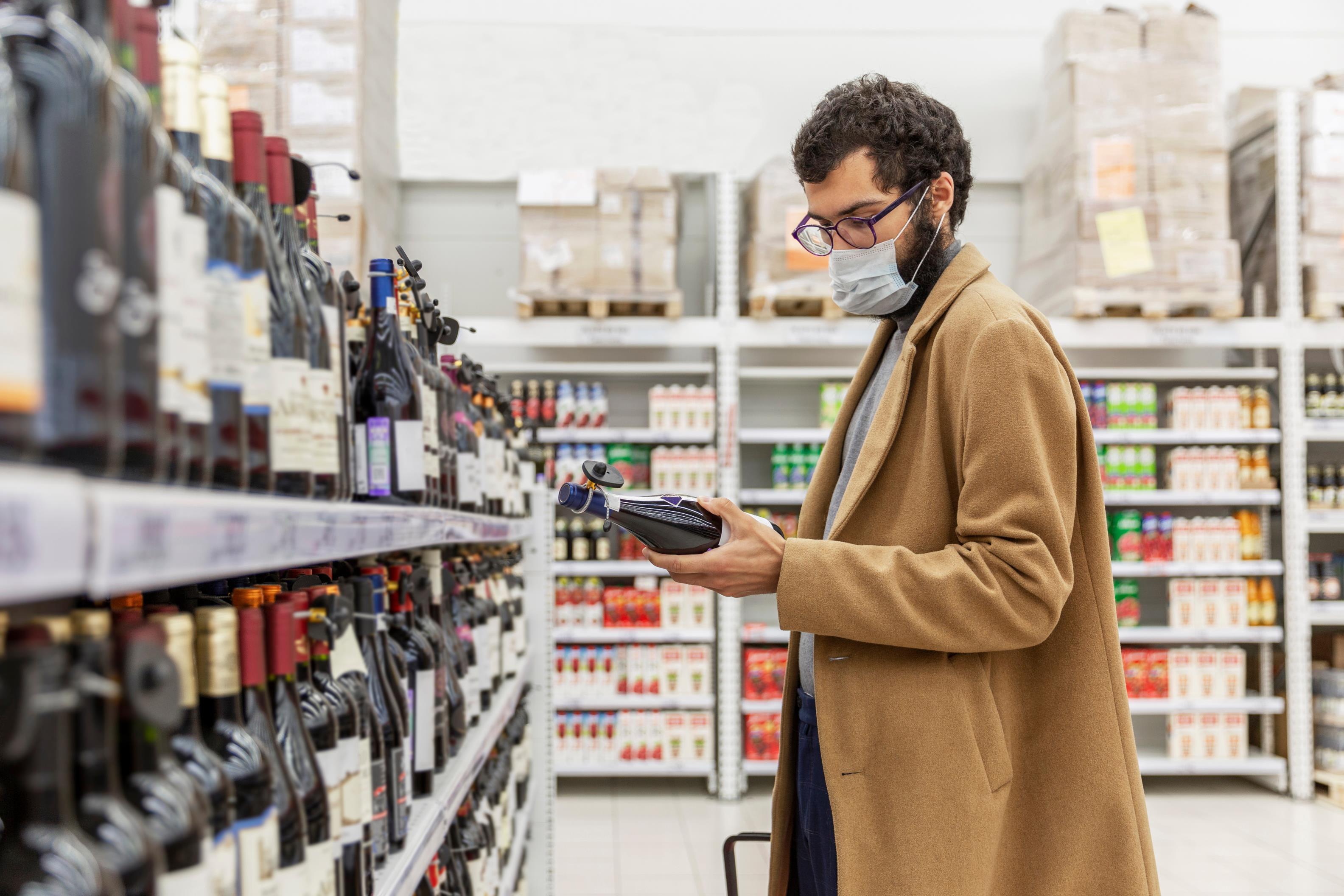 A man in a mask looking at a supermarket bottle of wine