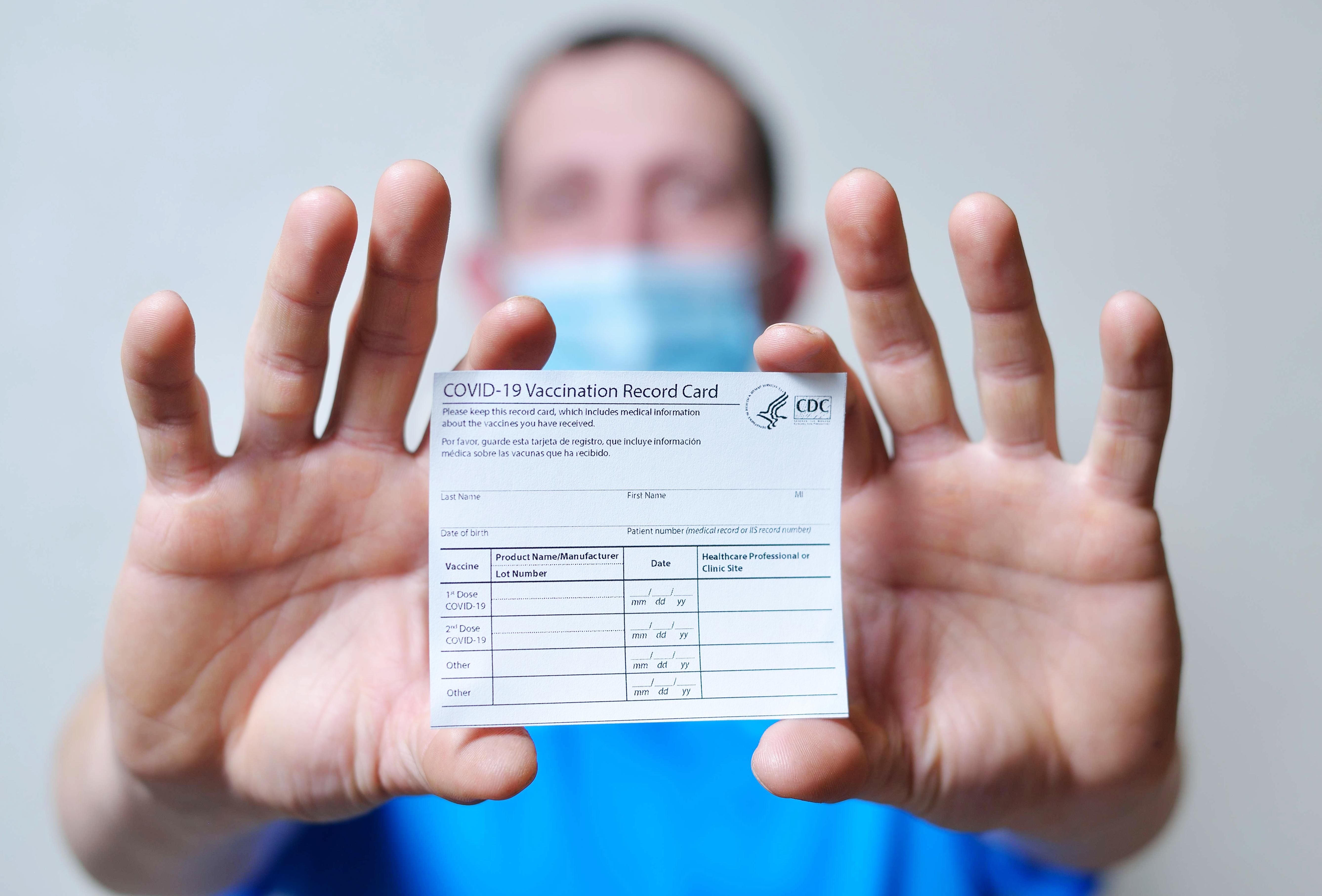 male is holding a vaccination record card and corona virus vaccine vials. Passport of immunity to the coro<em></em>navirus in the hands of a male. Health passport as proof of recovery from COVID-19.