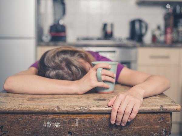 Person slumped over table asleep, clutching coffee mug