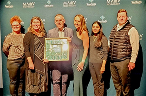 A group of 6 Kingston staff, with one in the centre holding the f<em></em>ramed MAV Award