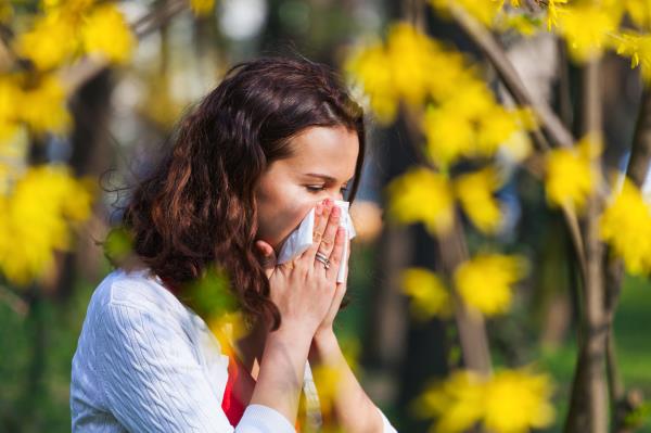 A woman blows her nose. She is outdoors.