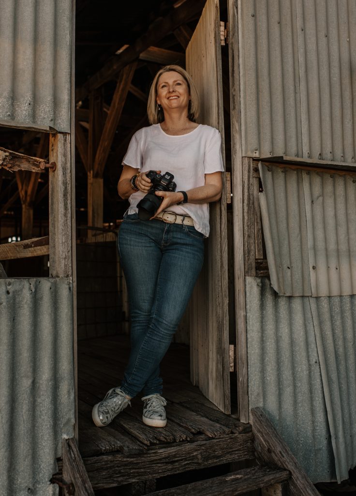 Photo of women in jeans and white t-shirt holding a camera in a wool shed.